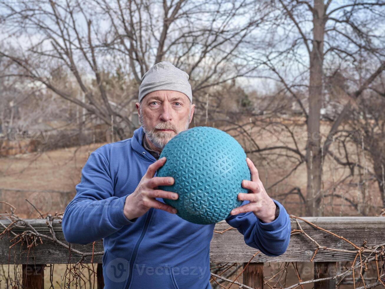 senior male is exercising with a heavy slam ball photo