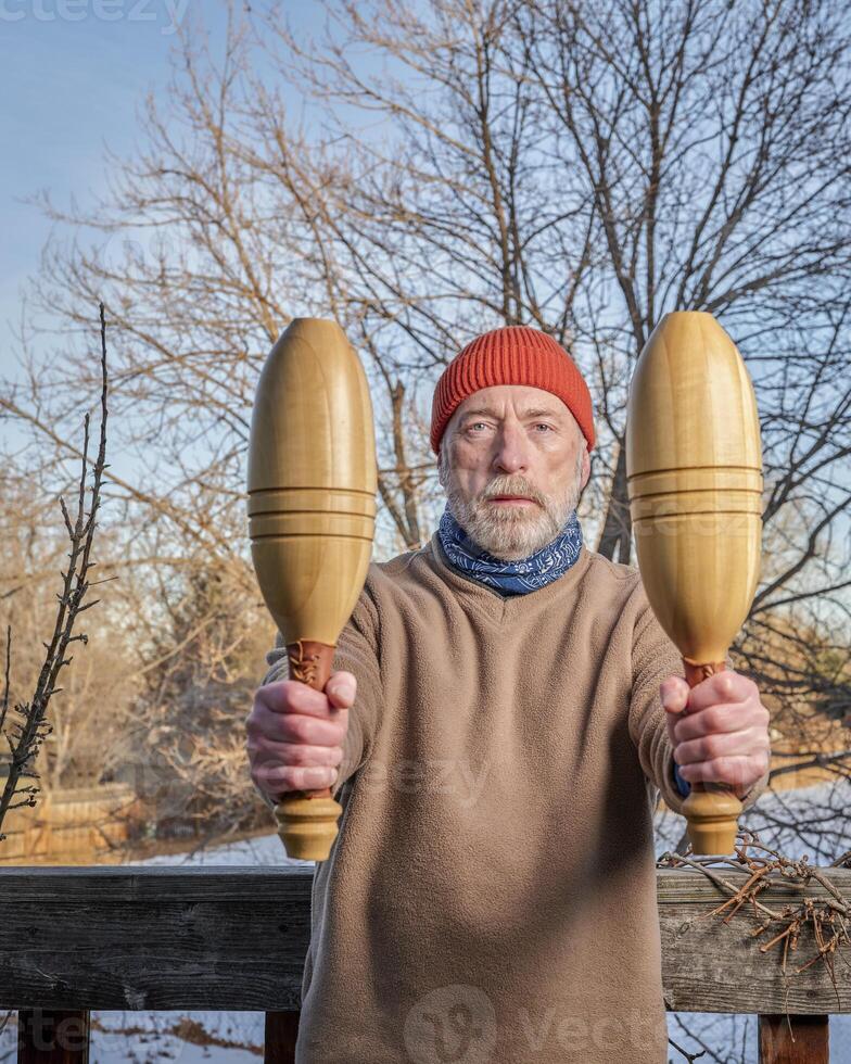 senior man is exercising with wooden Indian clubs photo