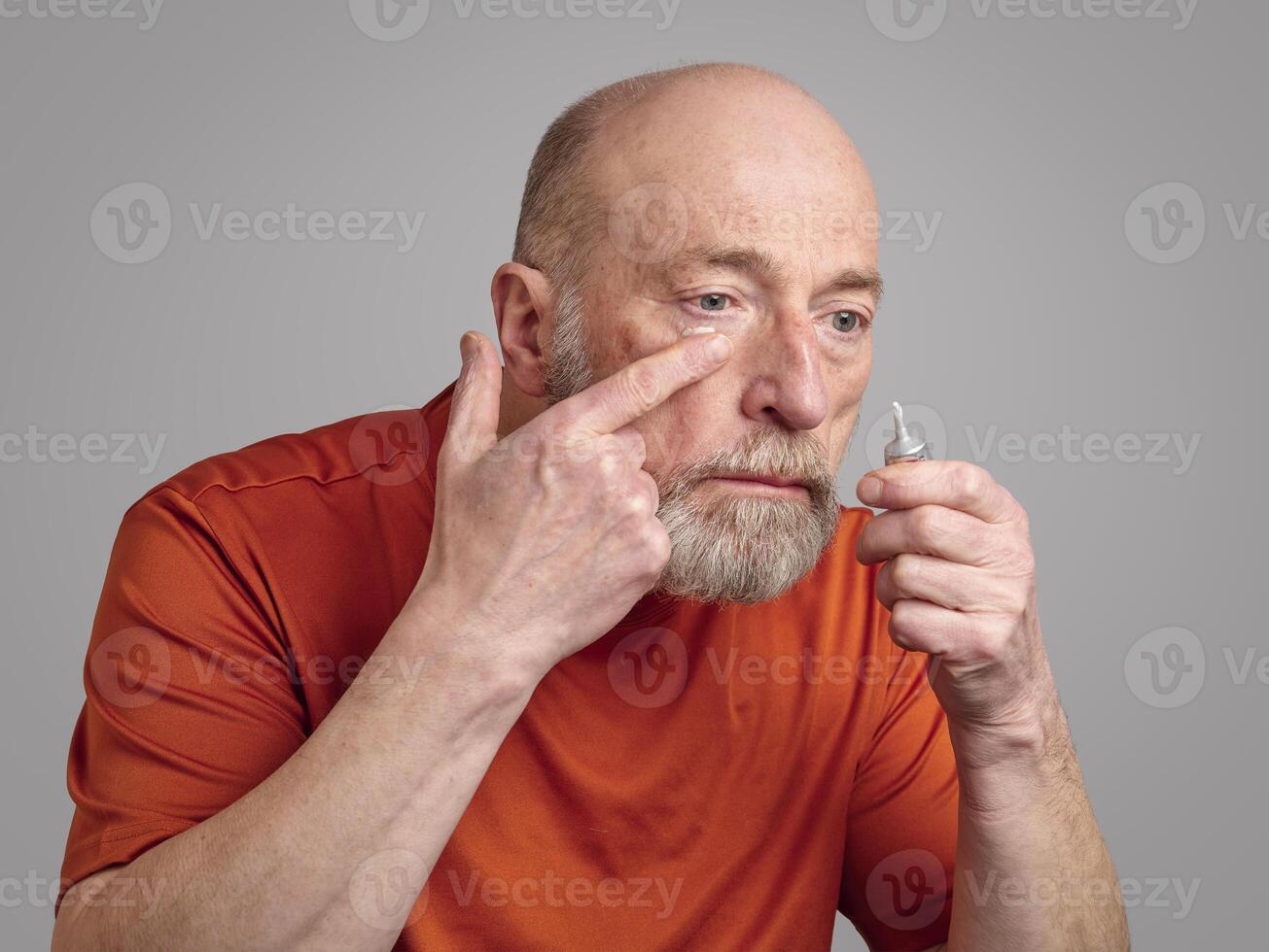 senior man is applying a retinol cream under his eyes photo