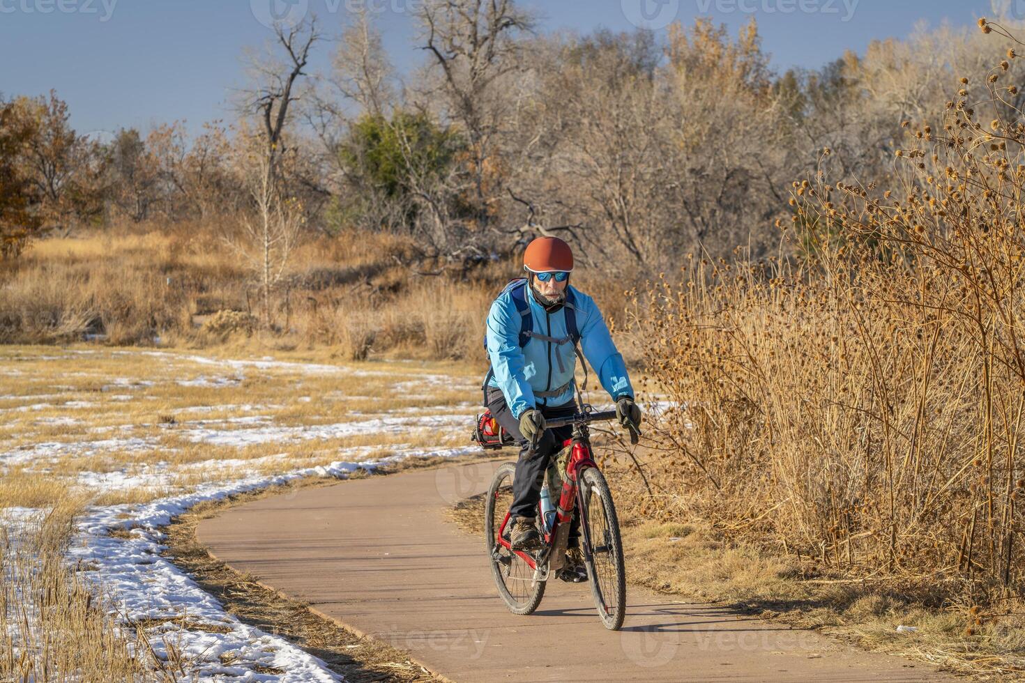 mayor masculino ciclista es montando un turismo grava bicicleta en un andar en bicicleta sendero en fuerte collins, Colorado en frío otoño clima con algunos nieve foto