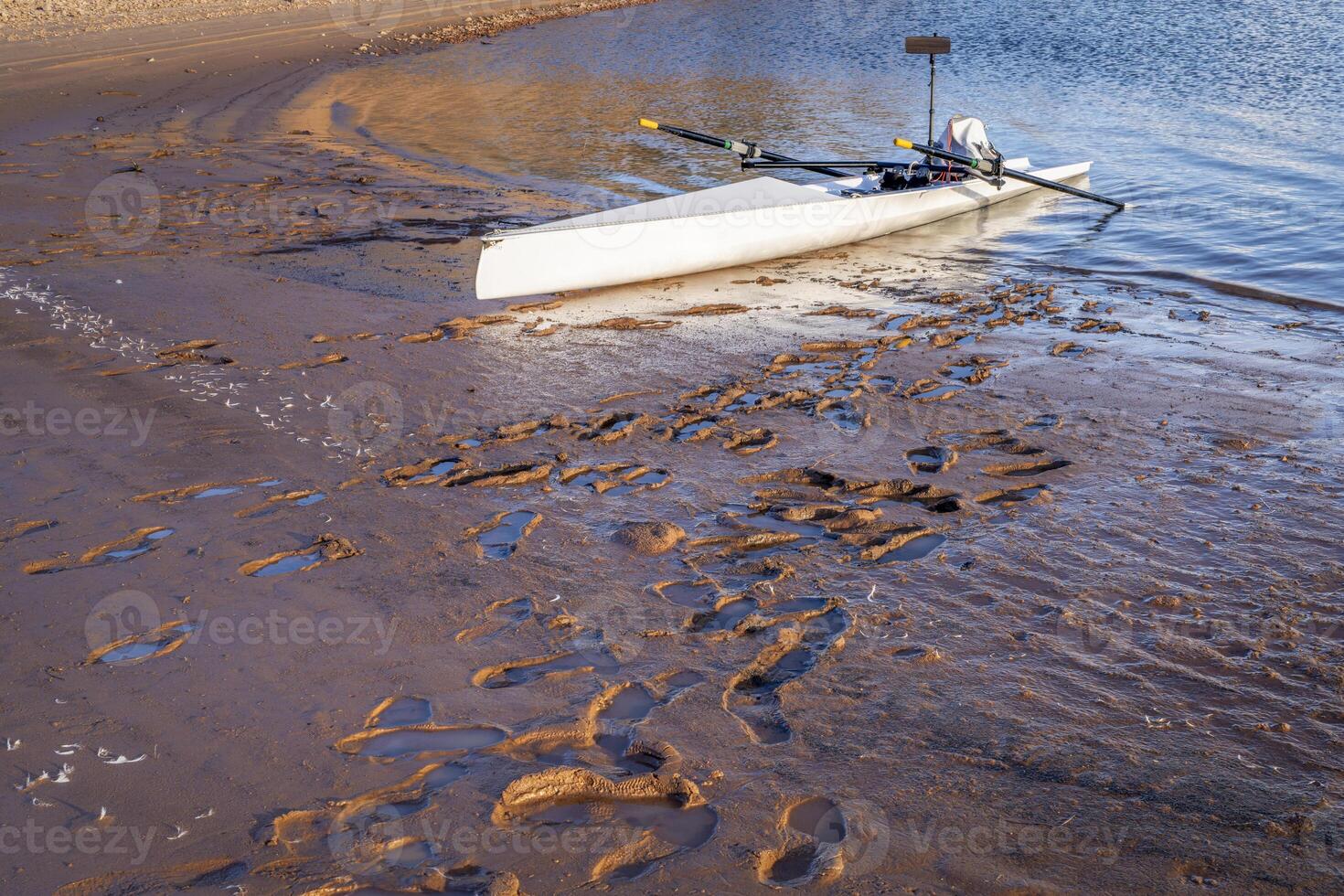 Coastal rowing shell on a muddy shore of Carter Lake in northern Colorado with footprints photo