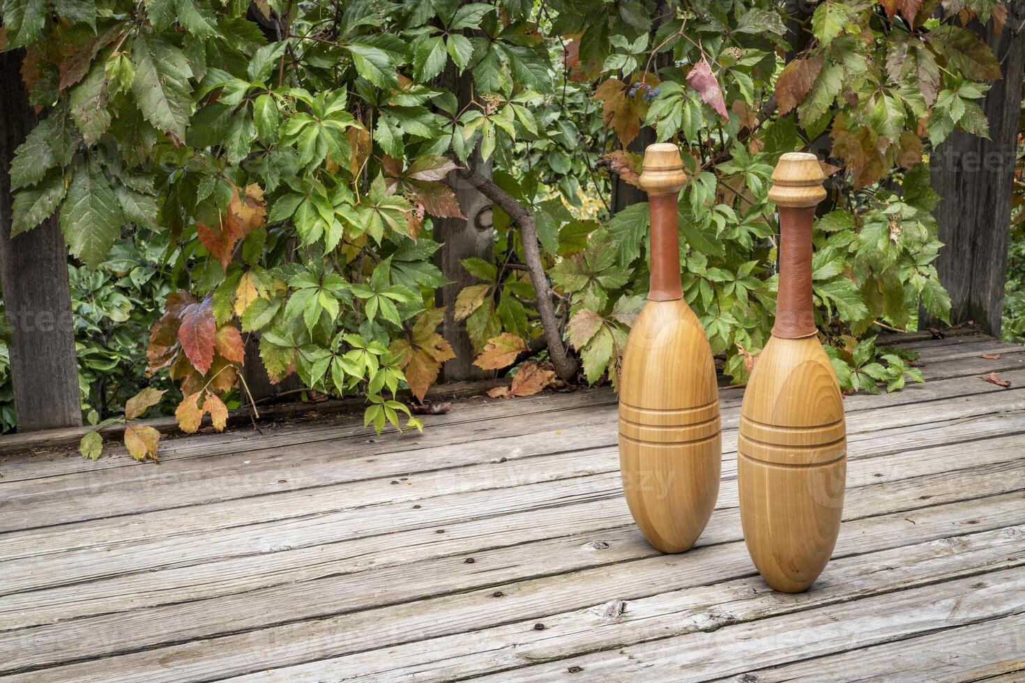 pair of wooden Indian exercise clubs on a wooden rustic deck, fall scenery photo