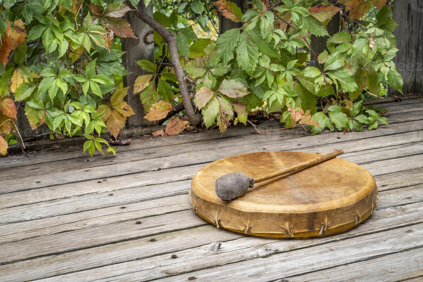 handmade, native American style, shaman frame drum covered by goat skin with a beater on a rustic wooden backyard deck photo