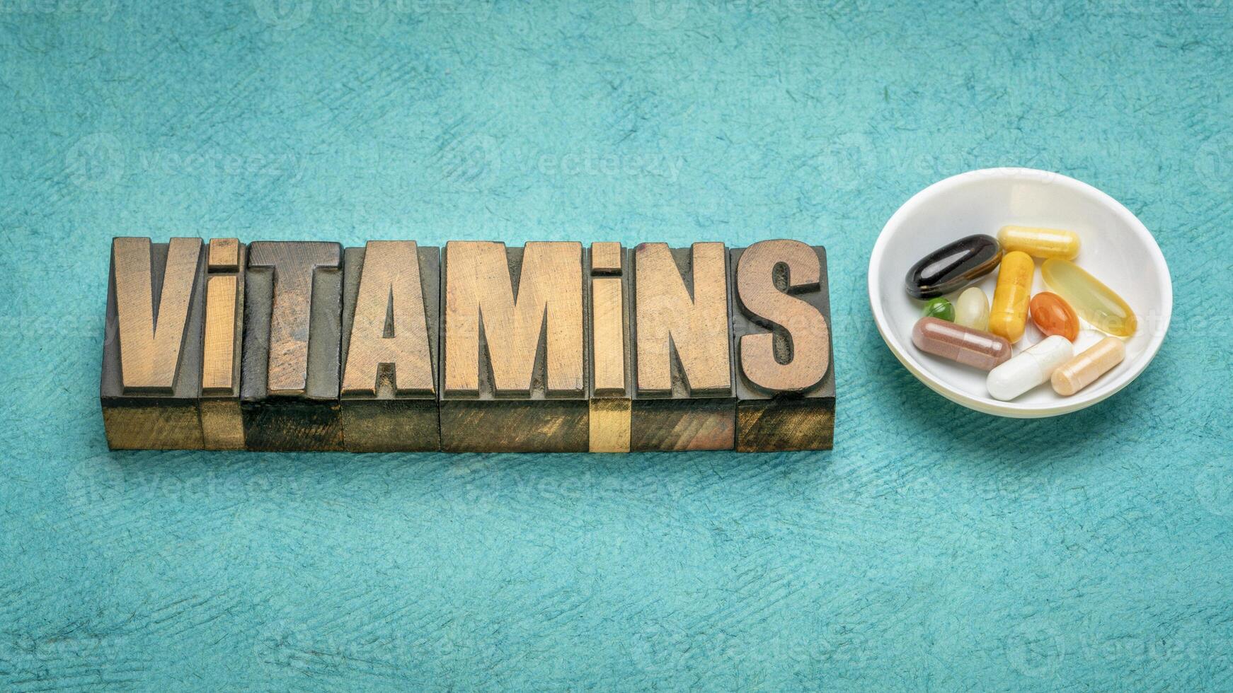 vitaminas palabra en Clásico tipografía madera tipo con un pequeño cuenco de pastillas y cápsulas, sano estilo de vida concepto foto