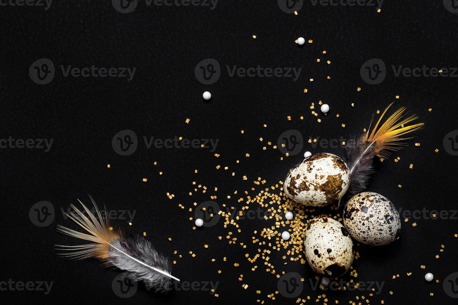 Moody easter background. Quail eggs, feathers and golden sugar sprinkles on black background. Happy easter holiday photo