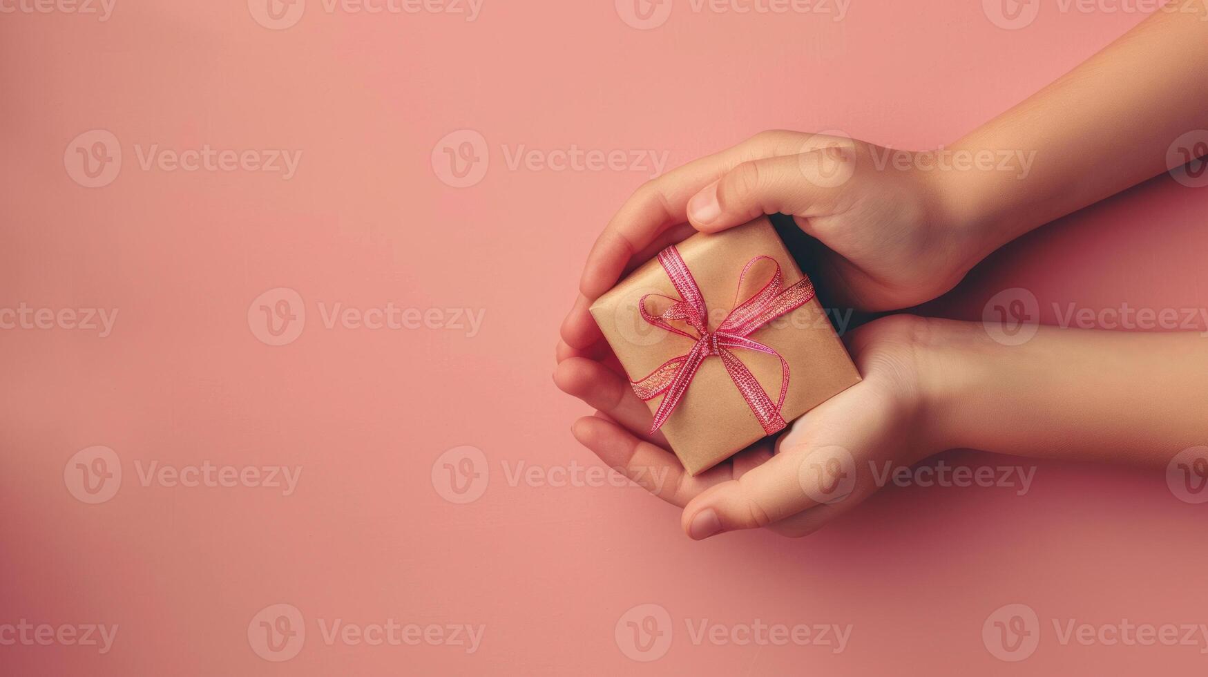 A person is holding a small gift box with a red ribbon on peach background photo