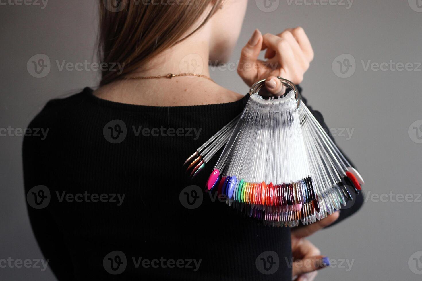 The girl holds in her hands a palette of samples of colored nail polishes. The face is not visible. Gray background. Nail color polish display. Choose the color of nail polish photo