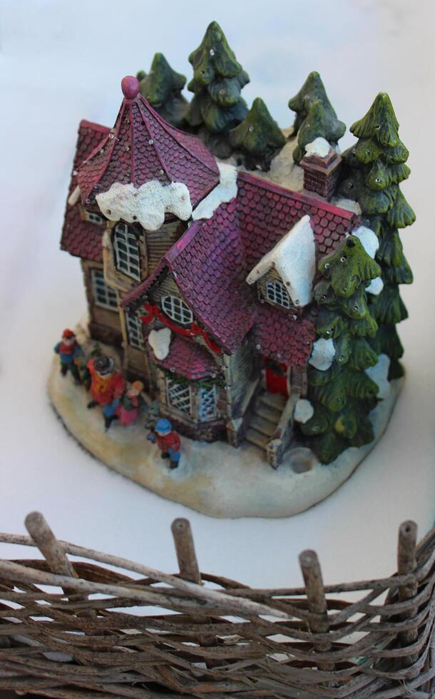 Figures of people on the porch of a toy house in the snow behind a wicker fence photo