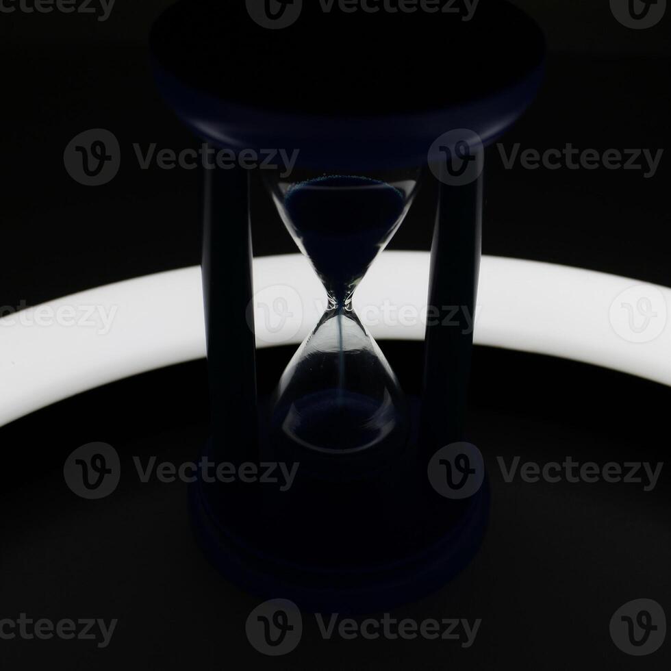 Illuminated Trickle Of Sand Inside Hourglass In Darkness Closeup View photo