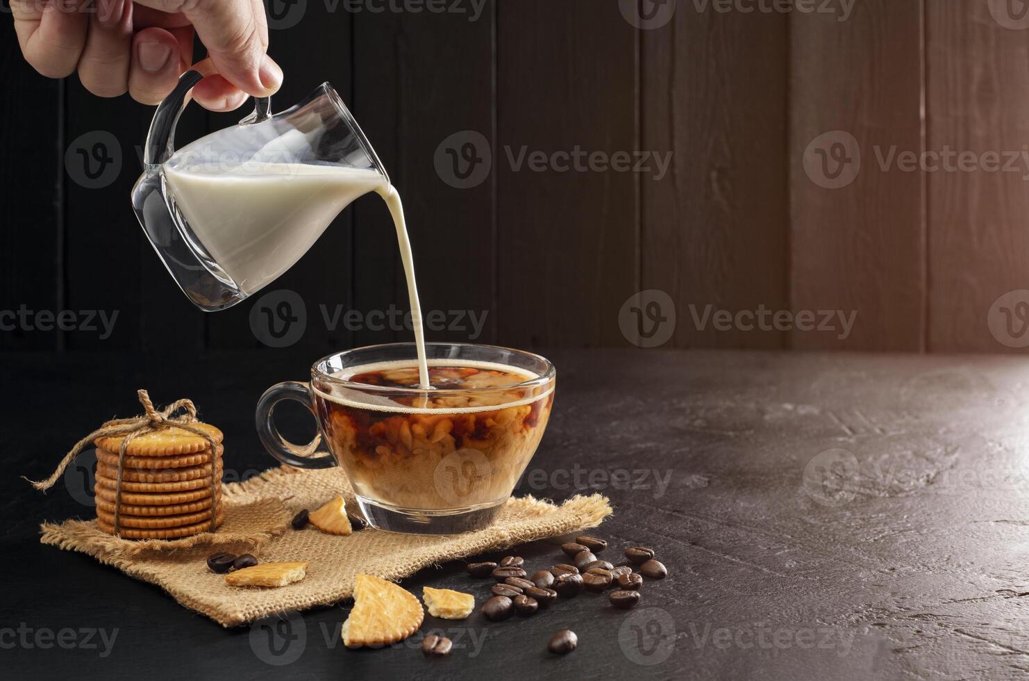 Milk cream poured into coffee cup, latte, cappuccino on wooden table black background and dark colors photo