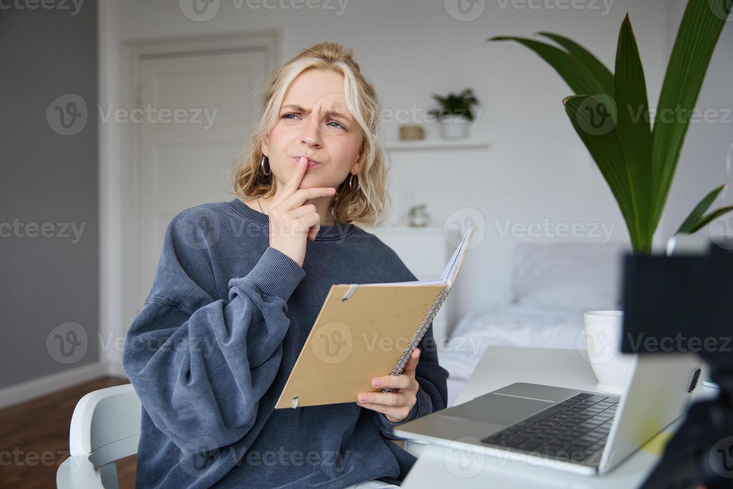 retrato de joven mujer, estudiante sentado en habitación, estudiando desde hogar, remoto educación concepto, participación cuaderno y pensamiento, mirando aparte con pensativo rostro, concentrando en asignación foto