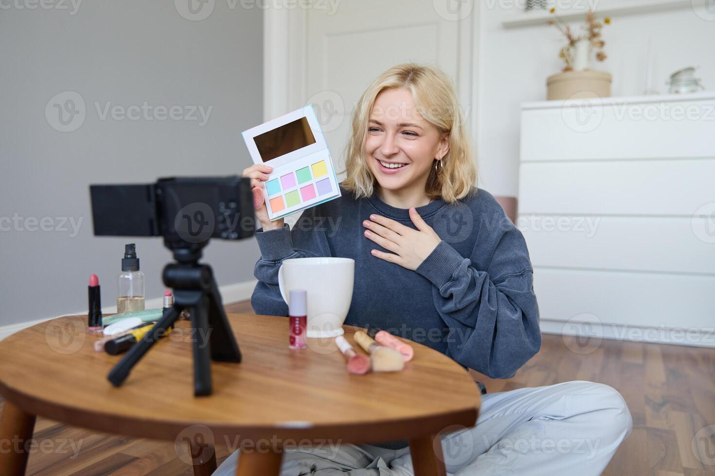 Portrait of beautiful smiling woman, recording in her room, has camera on coffee table, reviewing makeup, doing lifestyle vlog for social media account, records a tutorial photo