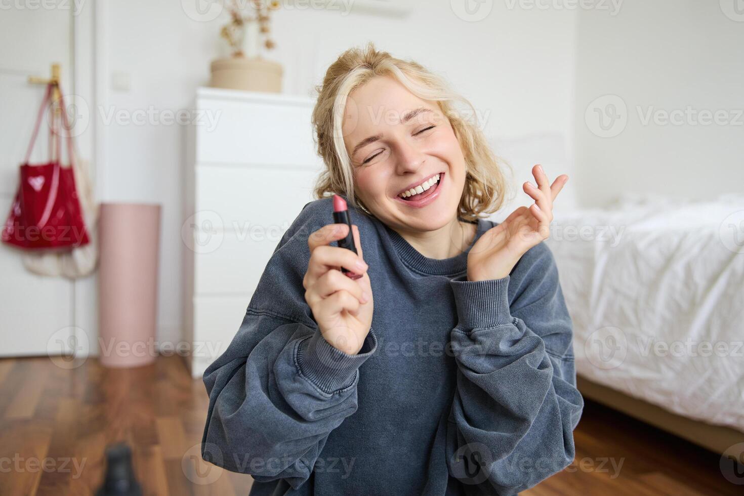 retrato de sonriente hermosa mujer en su habitación, sentado y demostración lápiz labial, recomendando favorito belleza producto, contenido fabricante grabación un de sí misma para social medios de comunicación Blog foto