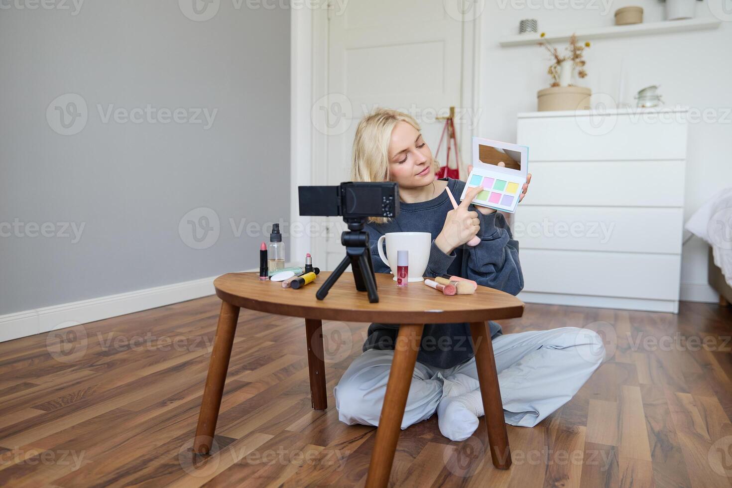 retrato de hermosa estilo de vida bloguero, niña registros un en su cámara para social medios de comunicación, muestra paleta de sombras de ojos, lo hace un maquillaje tutorial para su seguidores, se sienta en su habitación foto