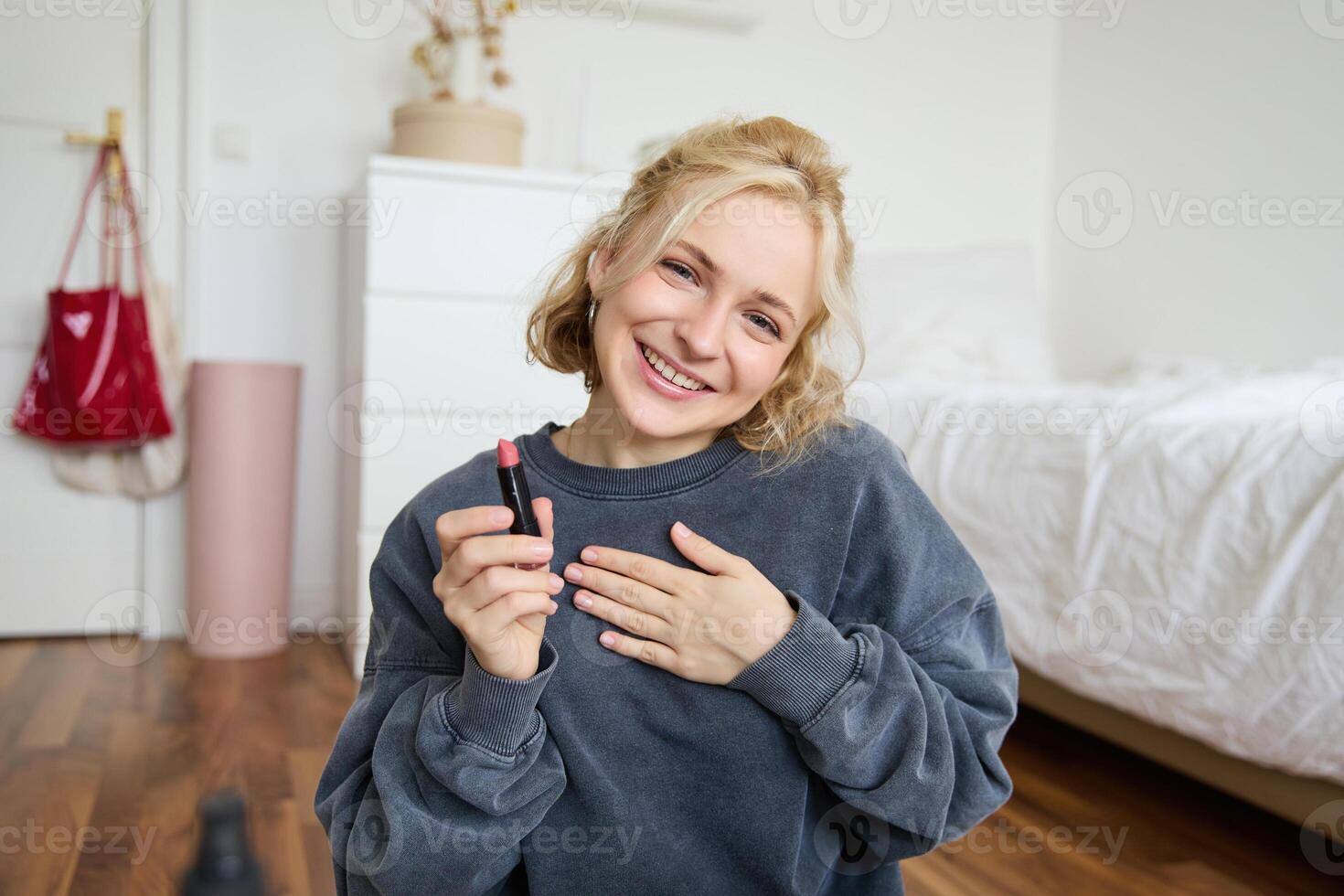 Portrait of cute, charismatic beauty blogger, woman sits in a room with lipstick in hand, talking about makeup, chatting with followers, recording online stream on social media app photo