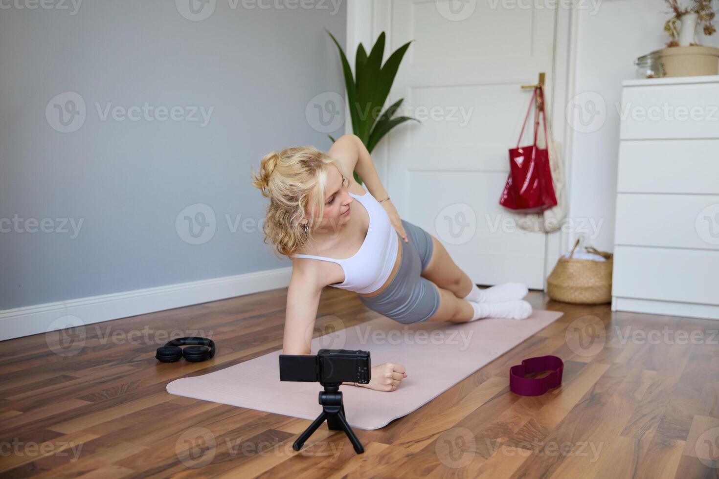 Portrait of young woman, fitness instructor recording of her standing in a side plank, doing workout at home on camera, creating content for social media photo