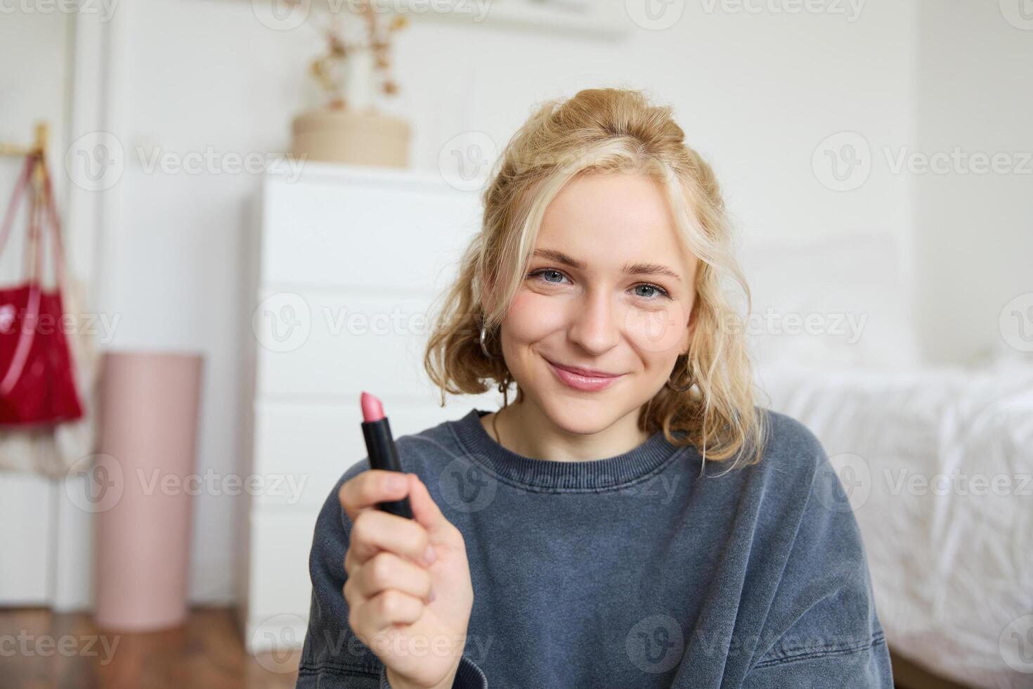 retrato de sonriente hermosa mujer en su habitación, sentado y demostración lápiz labial, recomendando favorito belleza producto, contenido fabricante grabación un de sí misma para social medios de comunicación Blog foto