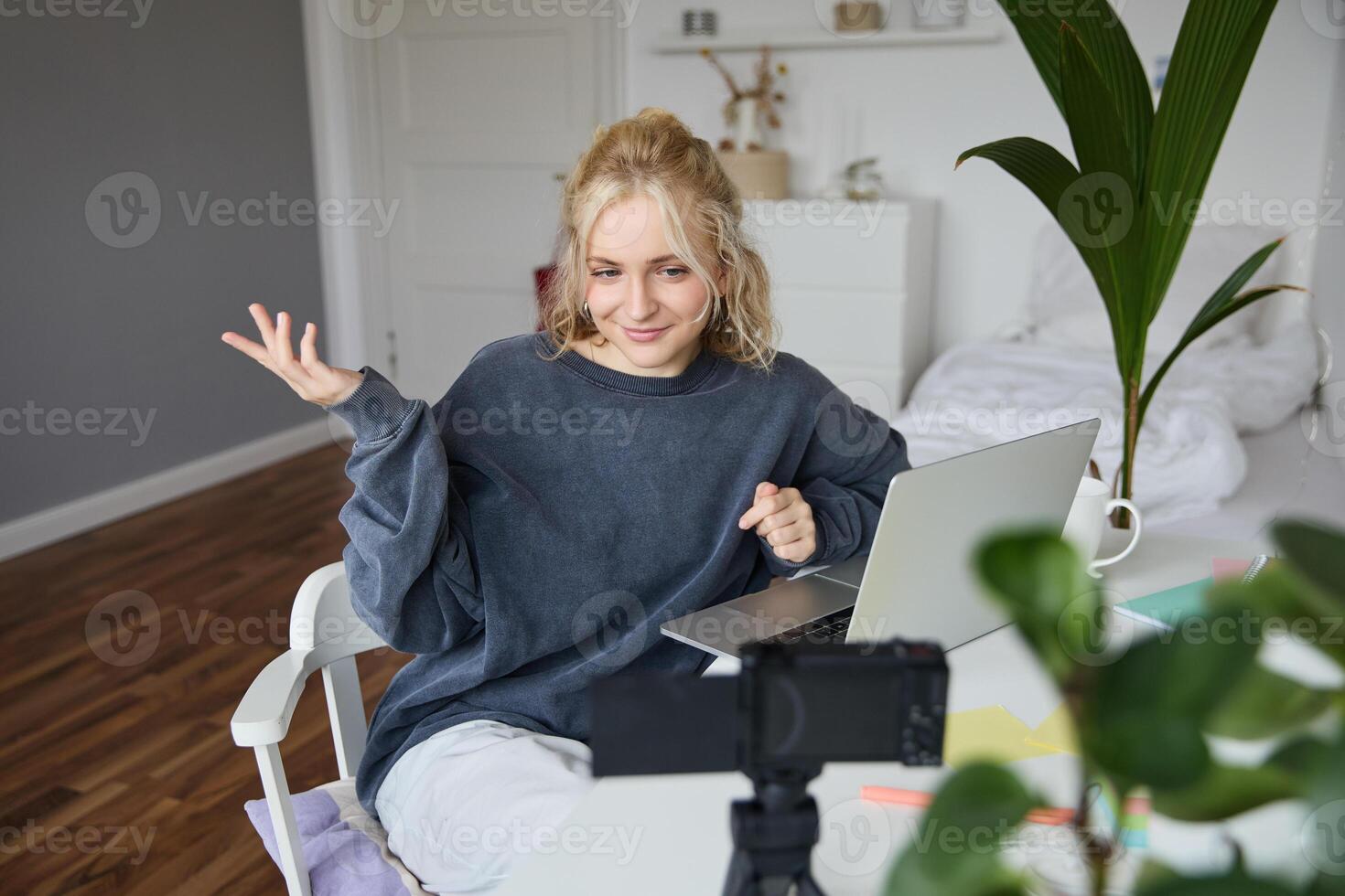 Portrait of young woman, lifestyle blogger, recording vlog about her life and daily routine, sitting in front of laptop, talking to followers, sitting in her room photo