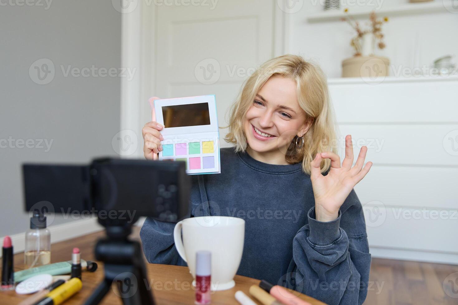 Portrait of beautiful smiling woman, recording in her room, has camera on coffee table, reviewing makeup, doing lifestyle vlog for social media account, records a tutorial photo