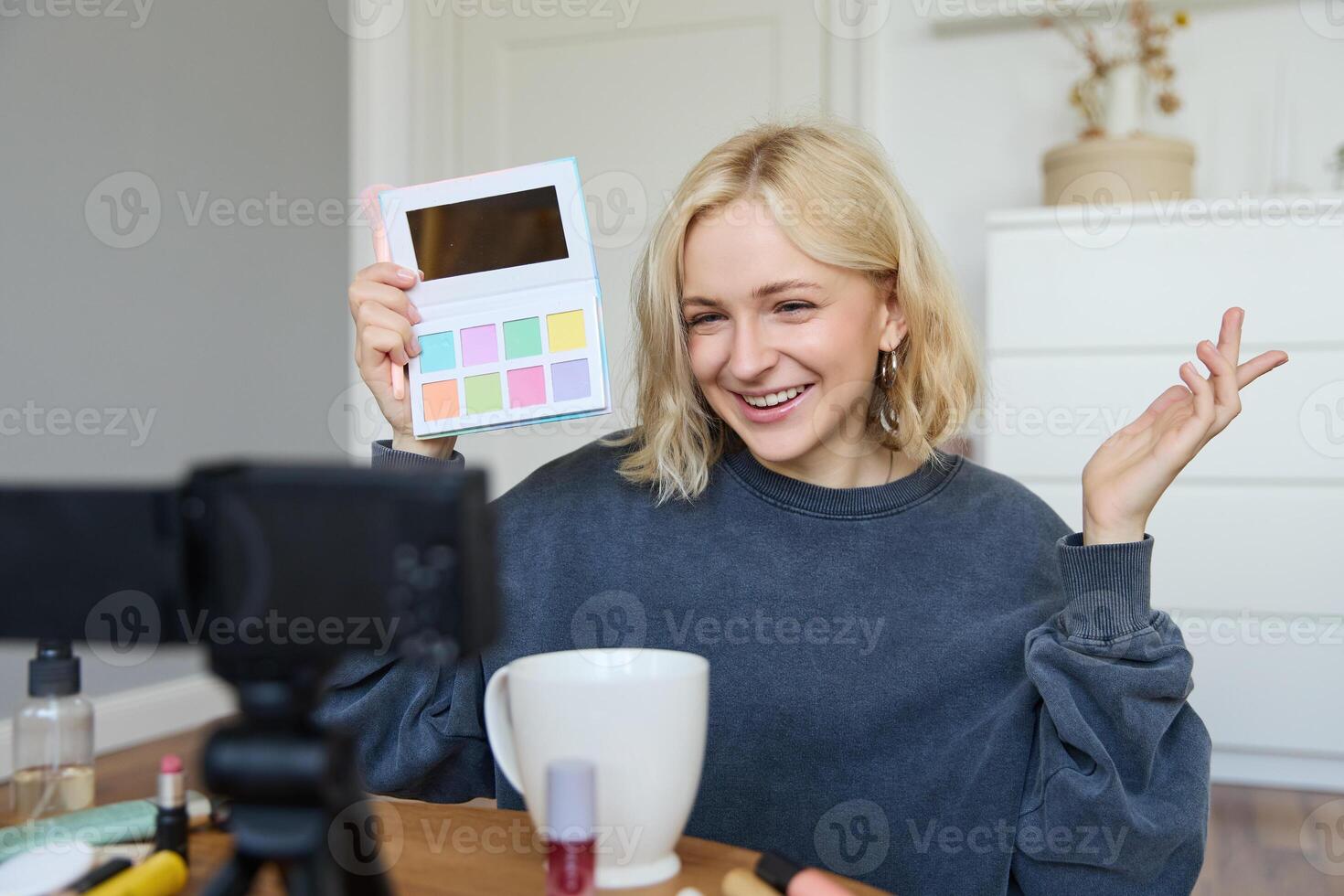 Portrait of beautiful lifestyle blogger, girl records a on her camera for social media, shows palette of eyeshadows, does a makeup tutorial for her followers, sits in her room photo