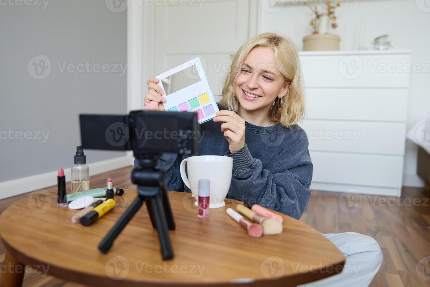 Portrait of beautiful smiling woman, recording in her room, has camera on coffee table, reviewing makeup, doing lifestyle vlog for social media account, records a tutorial photo