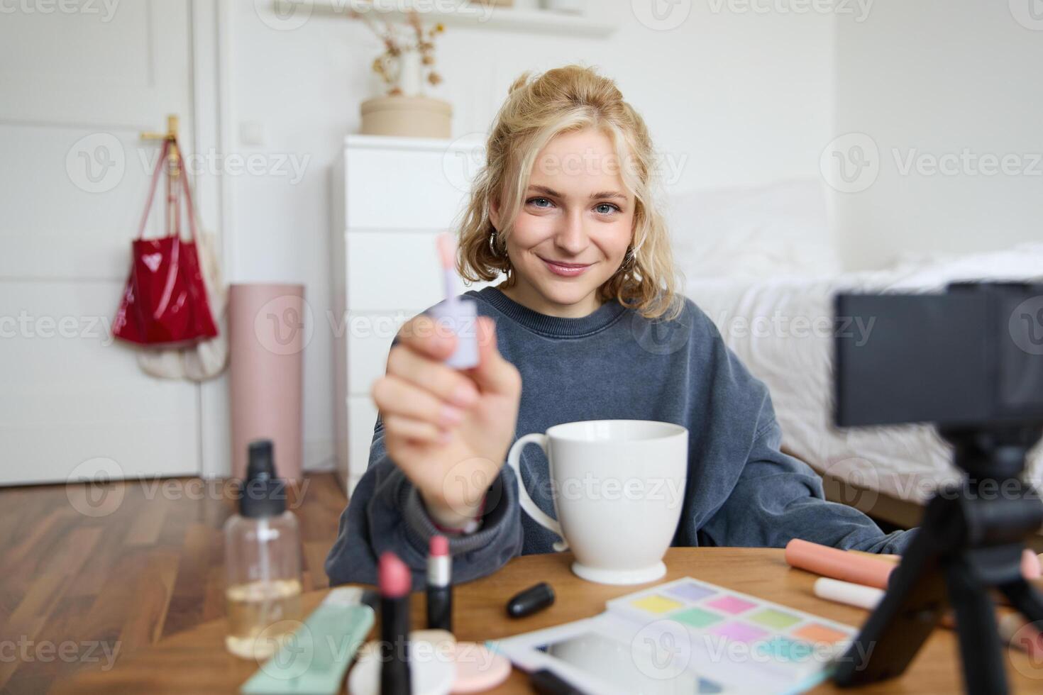 Portrait of smiling charismatic woman, puts on lip gloss, drinks tea, records on digital camera, beauty content for social media account photo