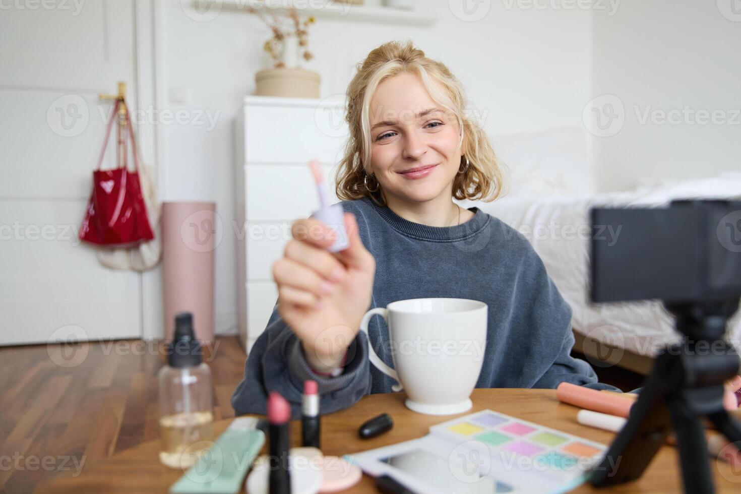 Lifestyle, beauty blogger, woman recording of her putting on makeup, talking to camera, making online tutorial, showing her lip gloss or lipstick to followers, sitting on floor with cup of tea photo