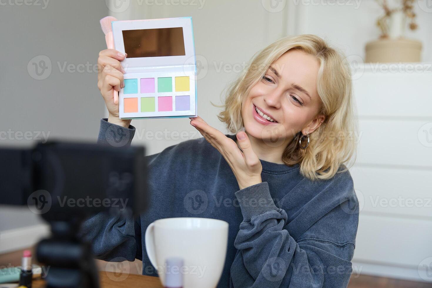 retrato de hermosa estilo de vida bloguero, niña registros un en su cámara para social medios de comunicación, muestra paleta de sombras de ojos, lo hace un maquillaje tutorial para su seguidores, se sienta en su habitación foto