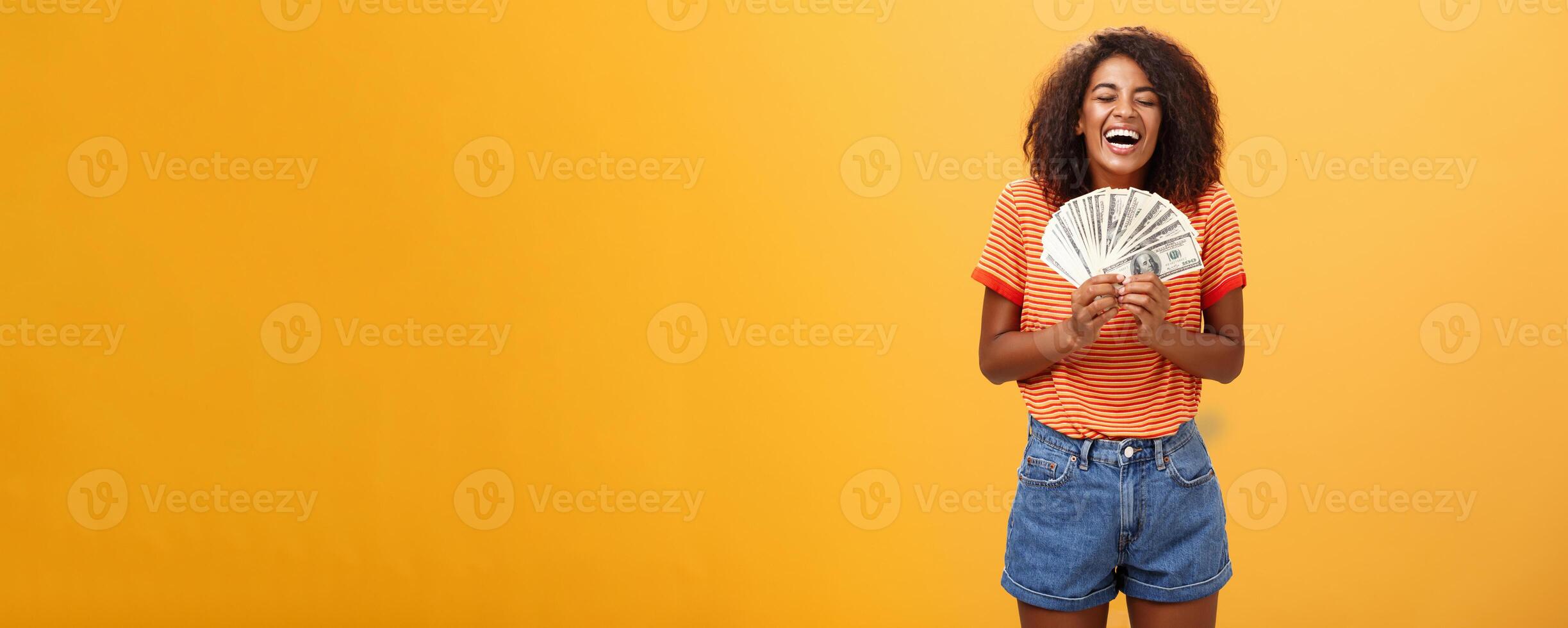 Finally girl rich. Portrait of happy charismatic stylish young female model receiving first payment holding lots of money and laughing from joy winning lottery ready waste cash over orange background photo