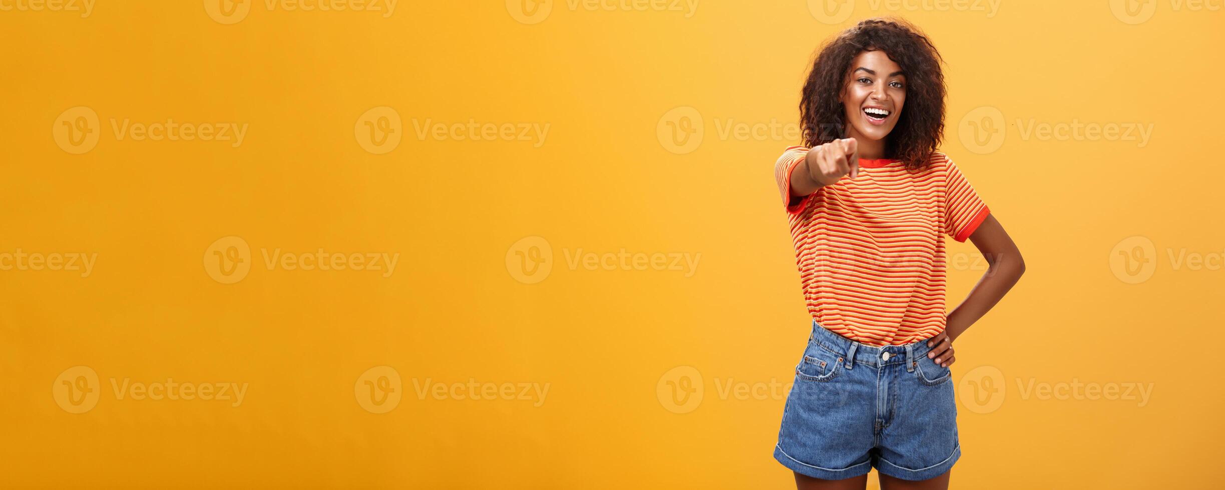 We hire you. Confident happy and awesome dark-skinned fashionable woman with curly hair holding hand on waist pointing at camera with index finger as if picking person or candidate, smiling photo