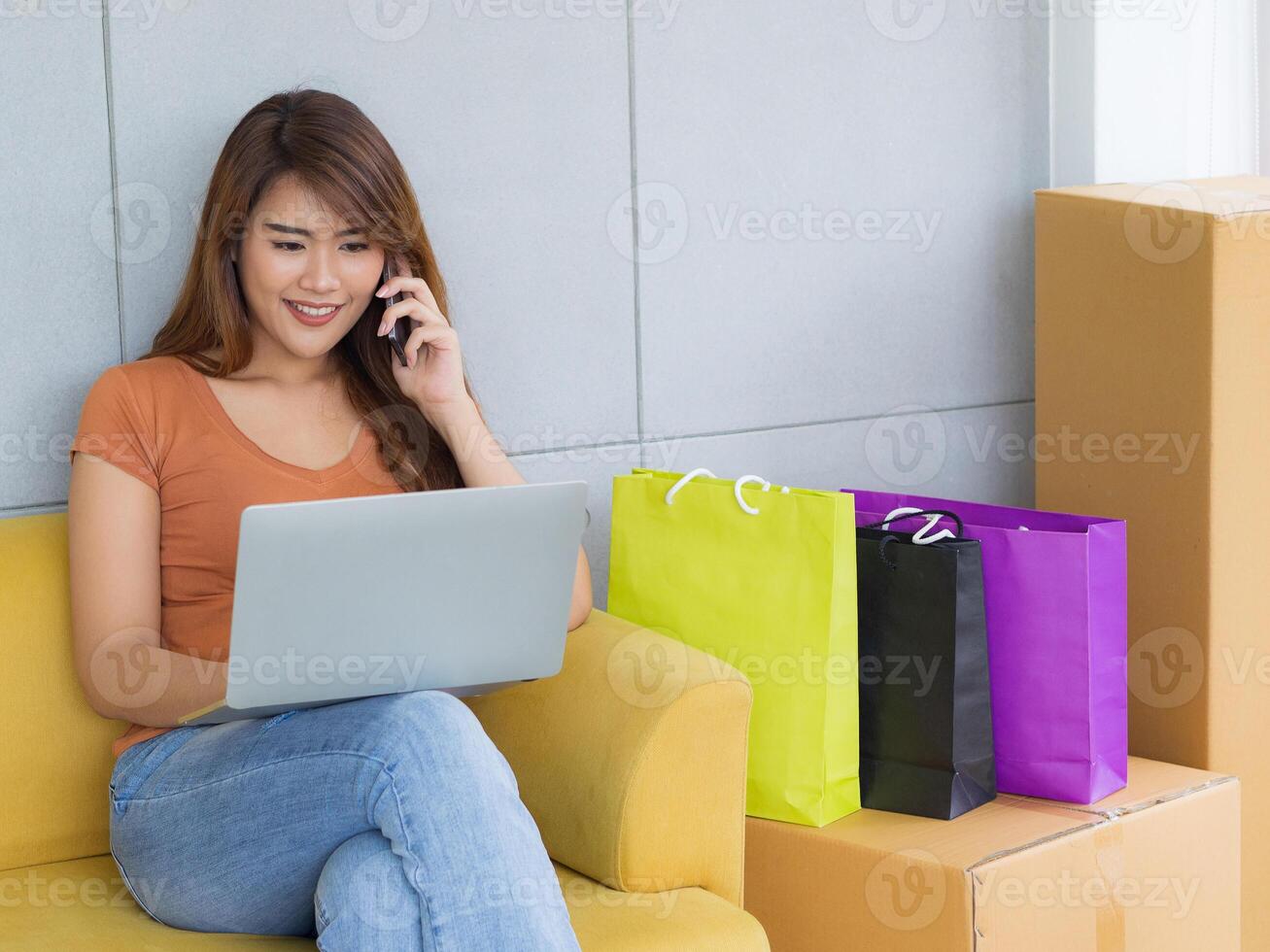 Businesswoman is e-commerce entrepreneur sitting at the chair talking on smartphone and lay the laptop on her leg in her office. Young woman's a negotiating about business. Business concept photo