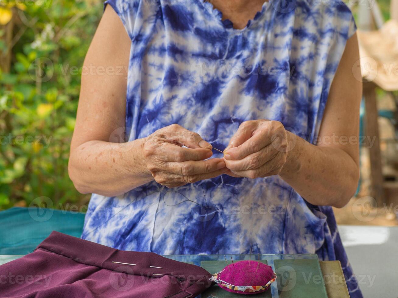 Close-up of hands senior woman's trying to thread a needle for sewing cloth. Space for text. Concept of aged people and relaxation photo