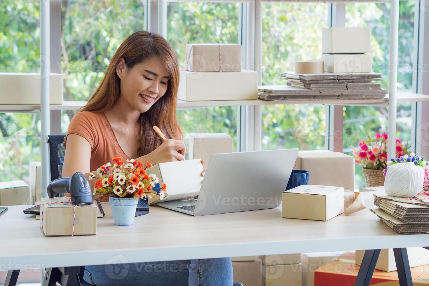 Businesswoman wears casual clothes sitting on a chair in the office. The work desk for an entrepreneur in the office has a laptop, barcode reader, and more. Space for text. Concept of business photo