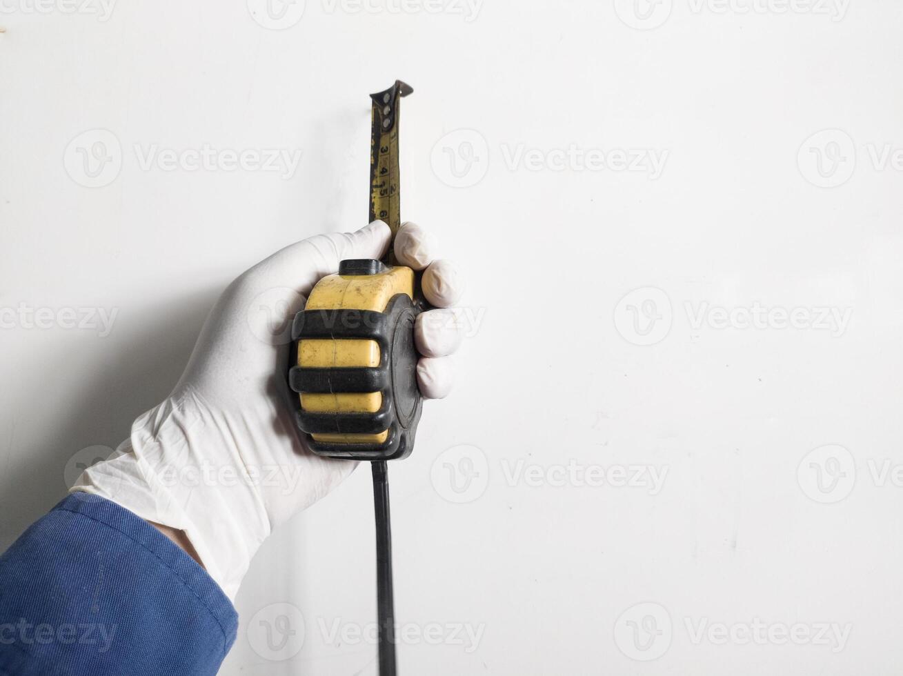 Man's hand with gloves holds a steel measuring tape yellow abnd black color isolated on white background. photo