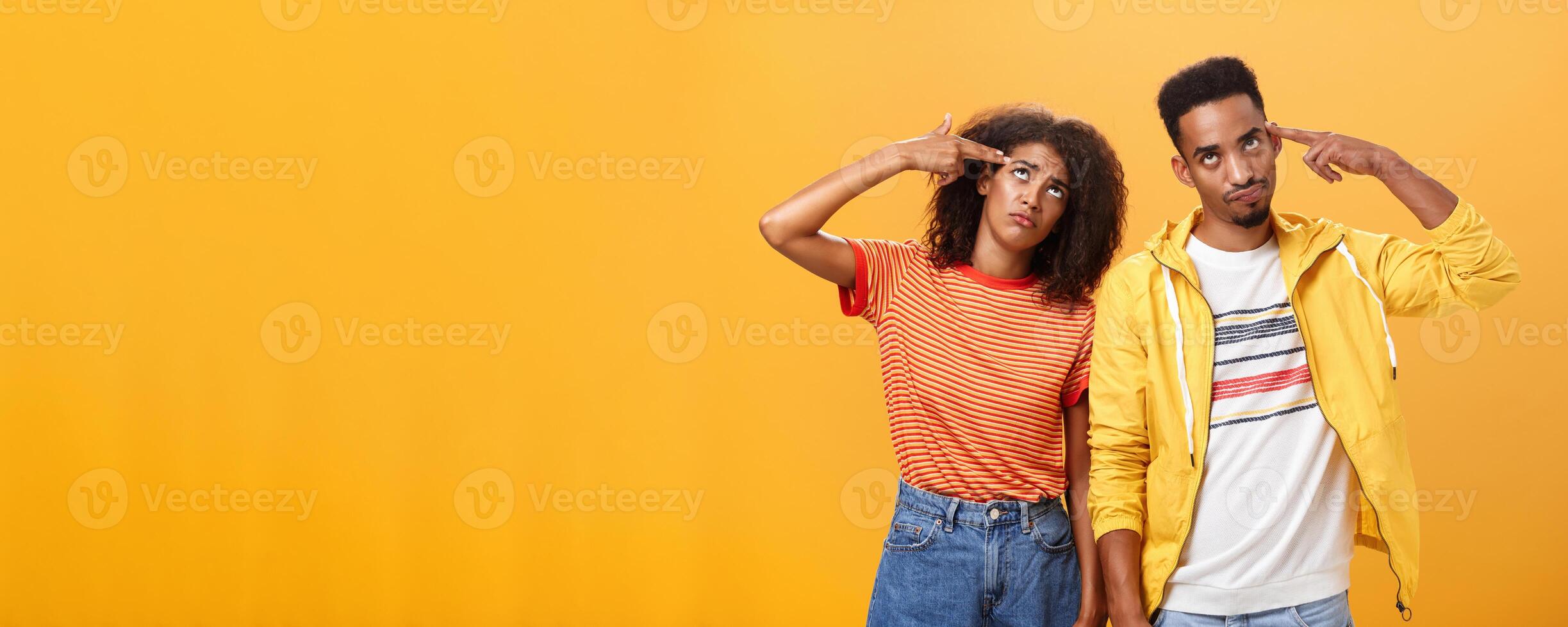 Pair of african american lovers getting annoyed with parents scolding, teaching them how live sexual life rolling eyes up from irritation holding finger gun near temples standing close to each other photo