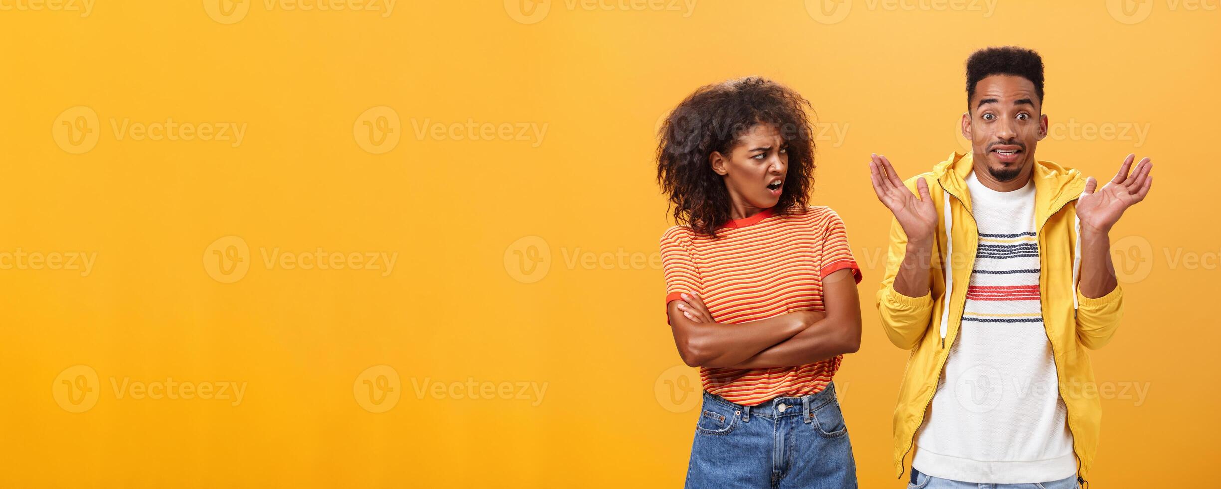 Jeez man what your problem. Offended displeased african american stylish and attractive girlfriend looking at boyfriend acting cool pretending he uninvolved shrugging with sorry look and smiling photo