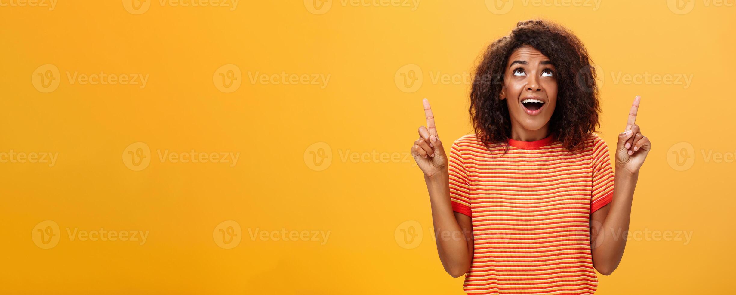 Optimistic happy african american girl saying thanks to god looking and pointing up pleased and carefree starting day in productive way being delighted with lucky chance over orange background photo