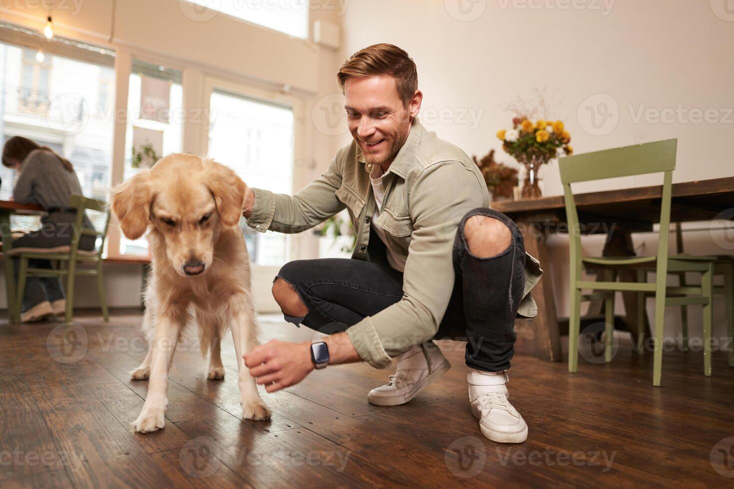 Portrait of happy man spending time with his dog in pet-friendly cafe, playing and petting golden retriever, having fun, giving him a treat photo