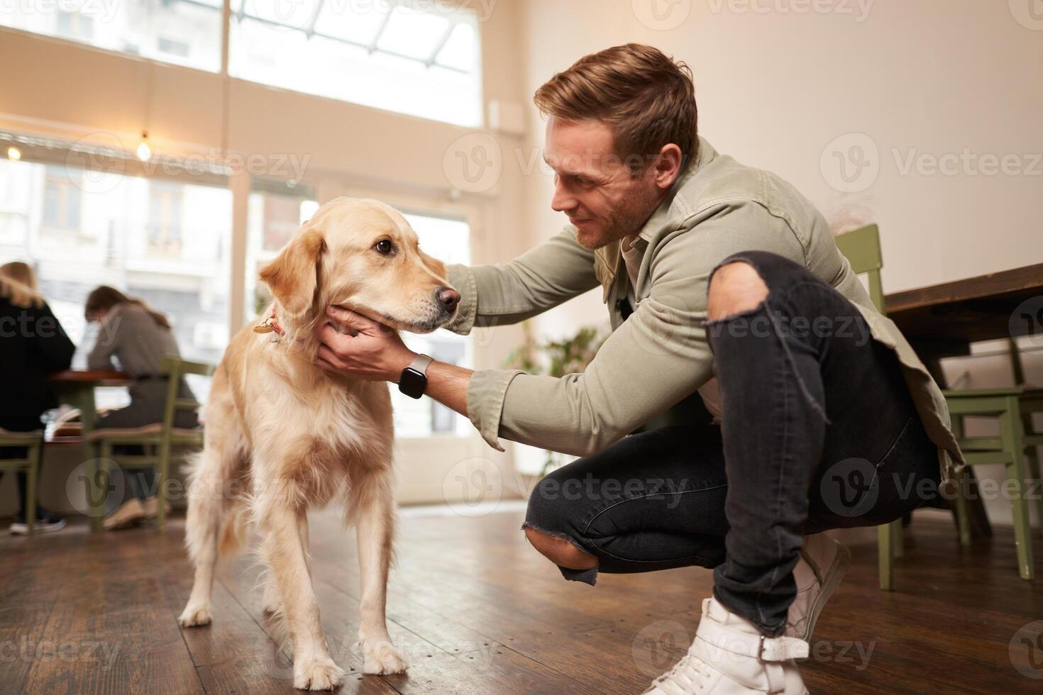 Close up portrait of handsome happy man petting his cute dog in a pet-friendly cafe. Coffee shop visitor with his golden retriever photo