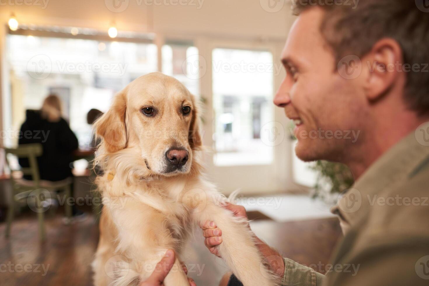 Close up portrait of young man with his pet in coffee shop. Dog owner playing with his pet, looking happy photo