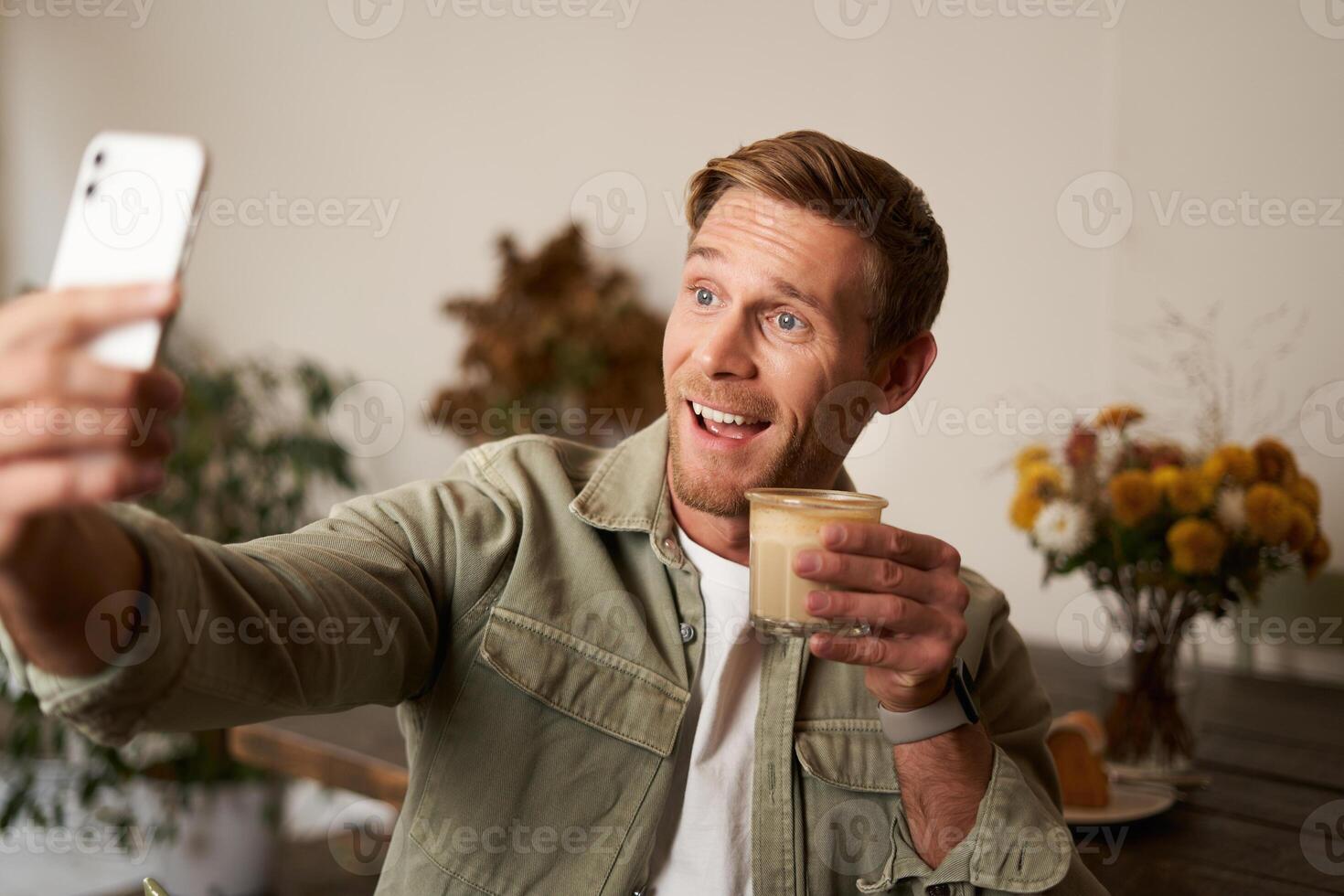Portrait of smiling handsome young man, chats with friend from cafe, doing selfies with cup of coffee photo