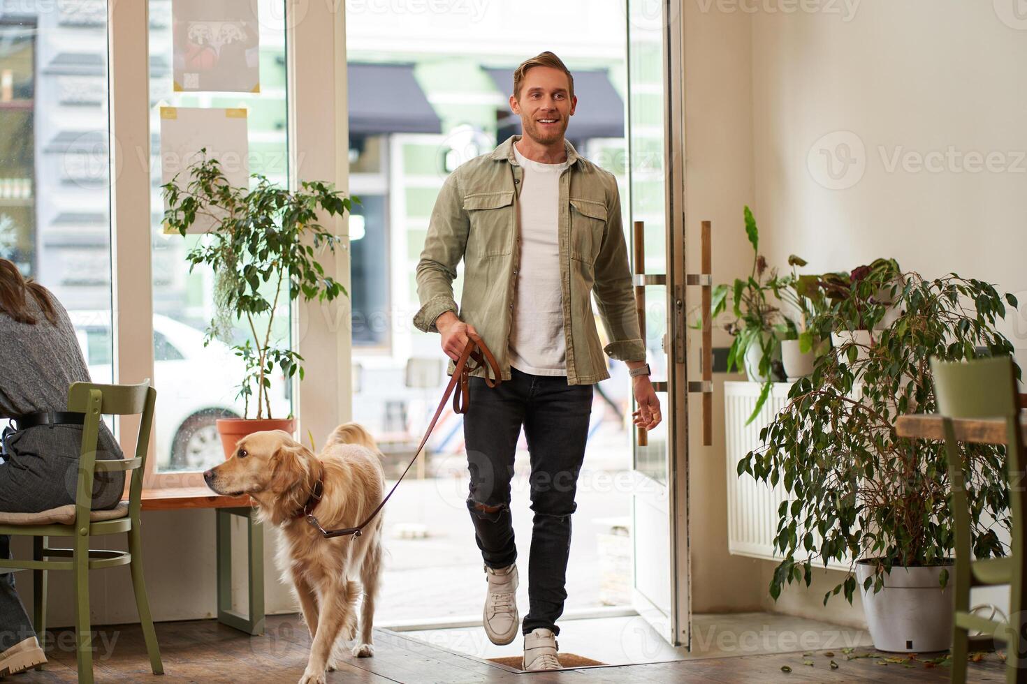 Portrait of handsome young man walks into the cafe with his dog on a leash, enters pet-friendly coffee shop, opens the door photo