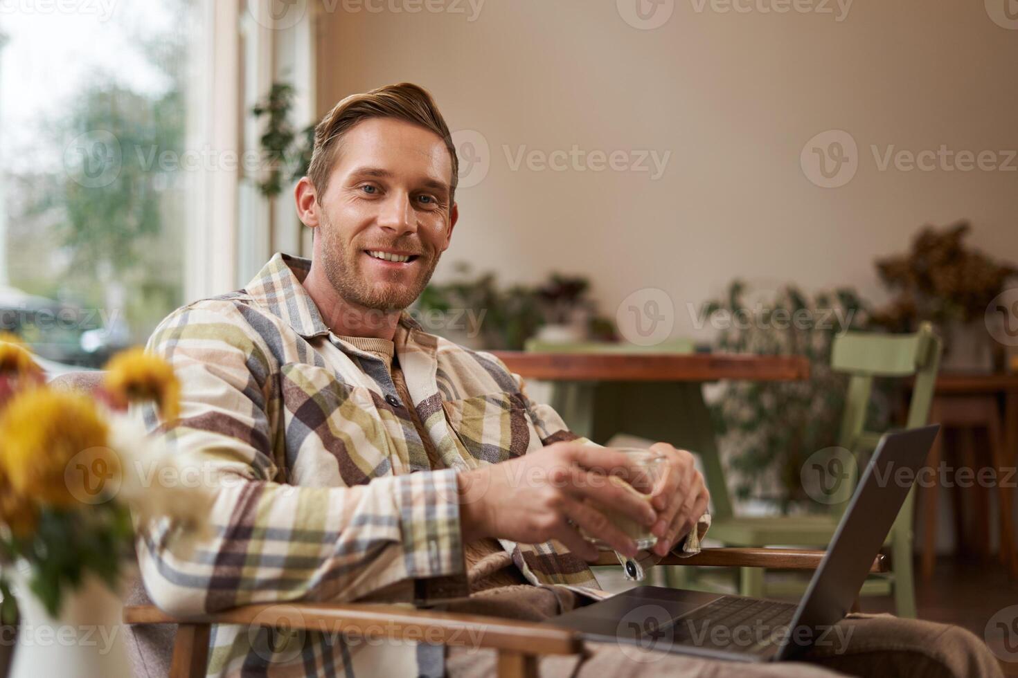 hermoso joven profesional, empresario sentado en café con vaso de café y trabajando en computadora portátil, buscando para inspiración fuera de de oficina espacio de trabajo foto