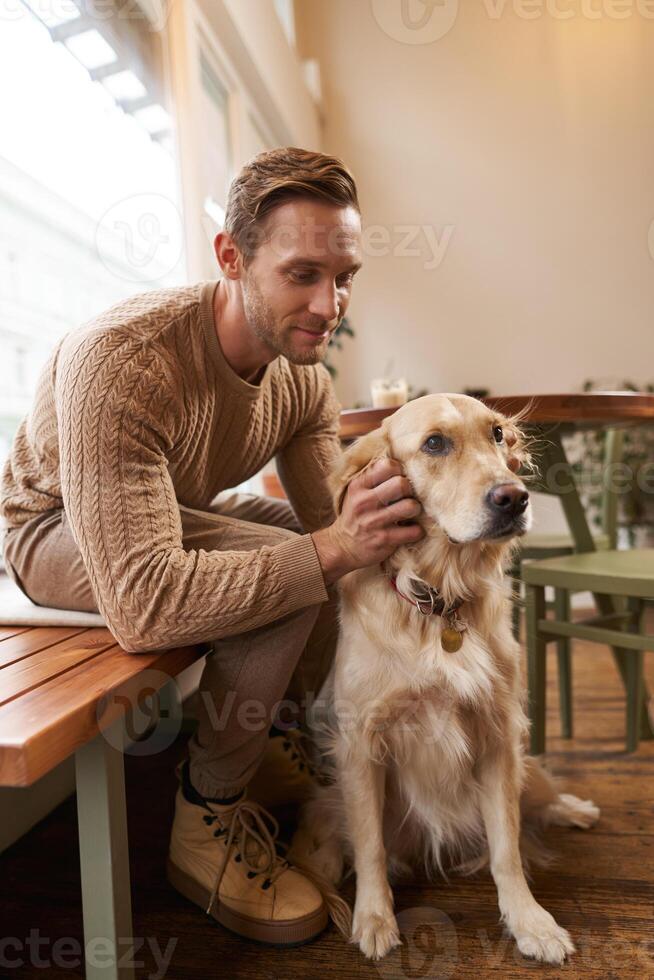 Close up portrait of handsome man with his dog, sitting in cafe. A guy drinks his coffee and touches golden retriever photo