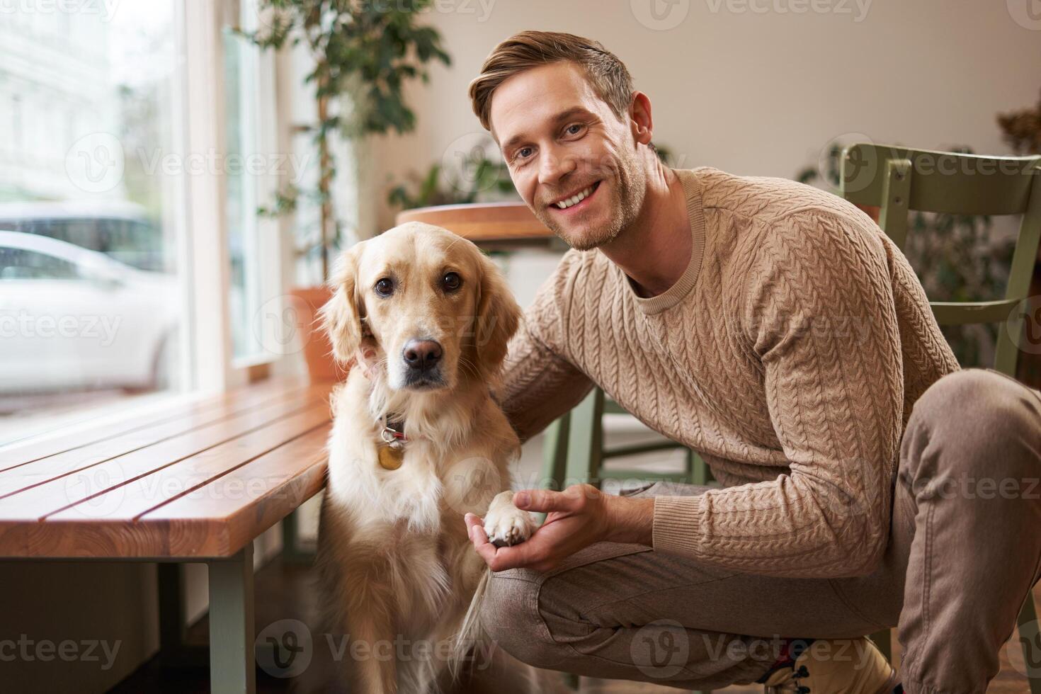 Portrait of a lovely golden retriever and handsome man in cafe. Cute dog gives paw and takes picture with his owner in coffee shop photo
