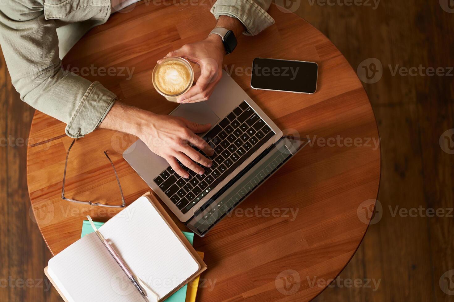 Co-working space, freelance and e-learning concept. Top view, male hands holding cup of coffee and using laptop. A man sitting in cafe and working or studying online photo