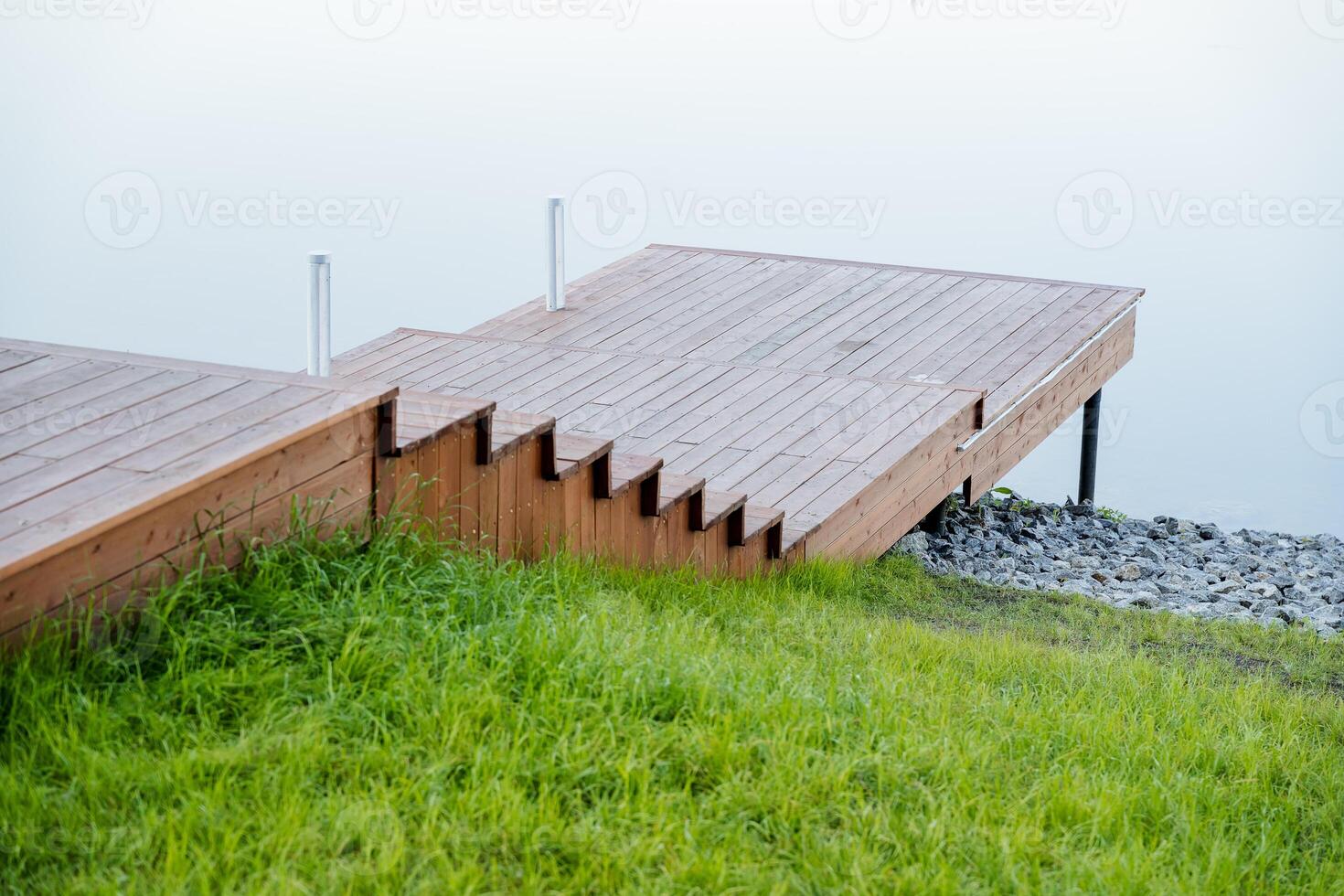 A wooden pier on the lake, a boardwalk to a pond, a river embankment, a city recreation park, parking for boats, a stone bank, a quiet place, a bridge to the river. photo