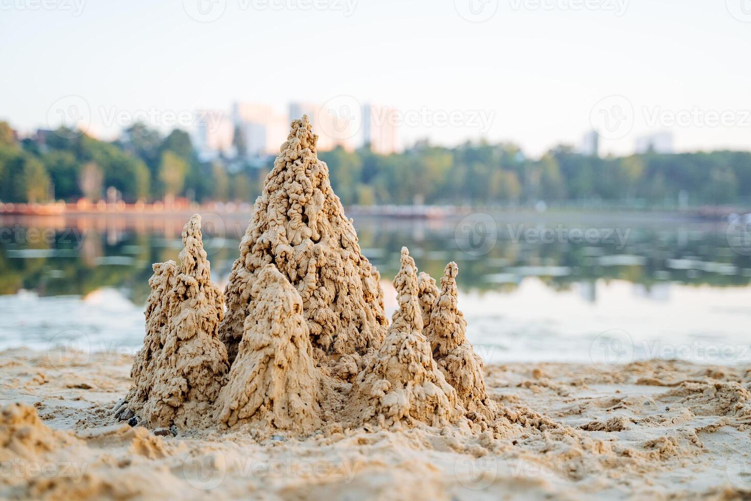 Wet sand lake shore, city recreation park, sand castle, sand drops, pond in the background, landscape in the morning. photo