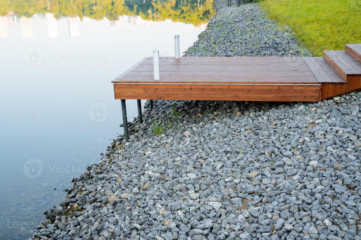 Boat dock in the city park, the stone bank of the river is covered with rubble, a wooden pier stands on stilts, a place to relax by the water, a rural pond photo