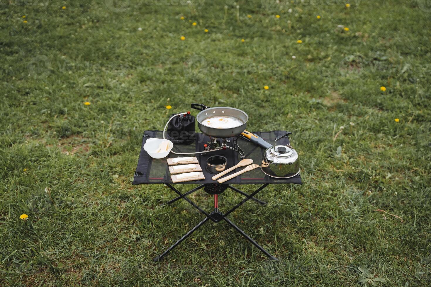 A tourist table with food on a hike stands against the background of grass, a folding camp kitchen, cooking in the fresh air, compact equipment for trekking, food on the table. photo